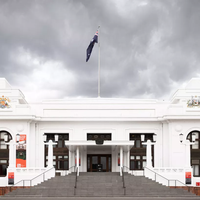 A large staircase leads up to a white old building with a flag on the top.