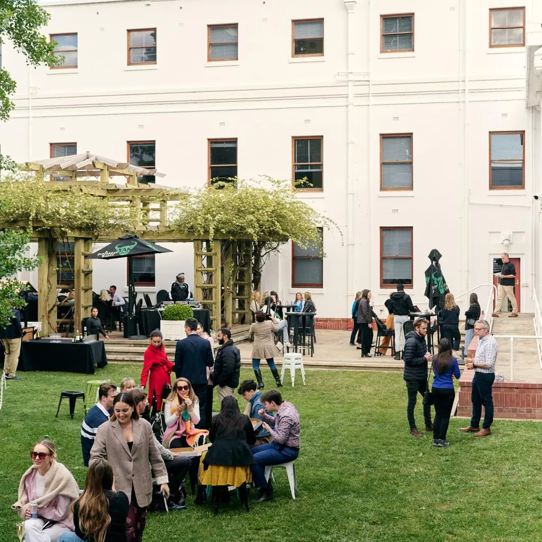 A large enclosed grassed area, the House of Representatives courtyard, with many groups of people gathered, talking, eating and drinking.