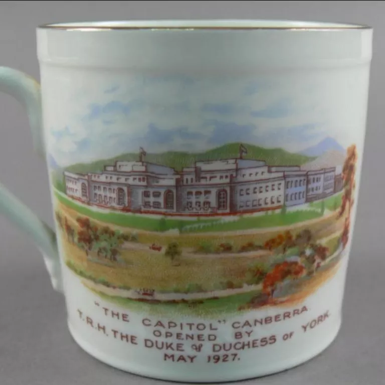 Souvenir mug from 1927, the front depicting parliament house surrounded by green hills and fields, the back showing a wreath with a kangaroo and the Australian and UK flags.