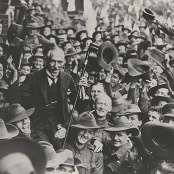 Prime Minister Hughes being held up by a crowd of returning soldiers in a busy street.