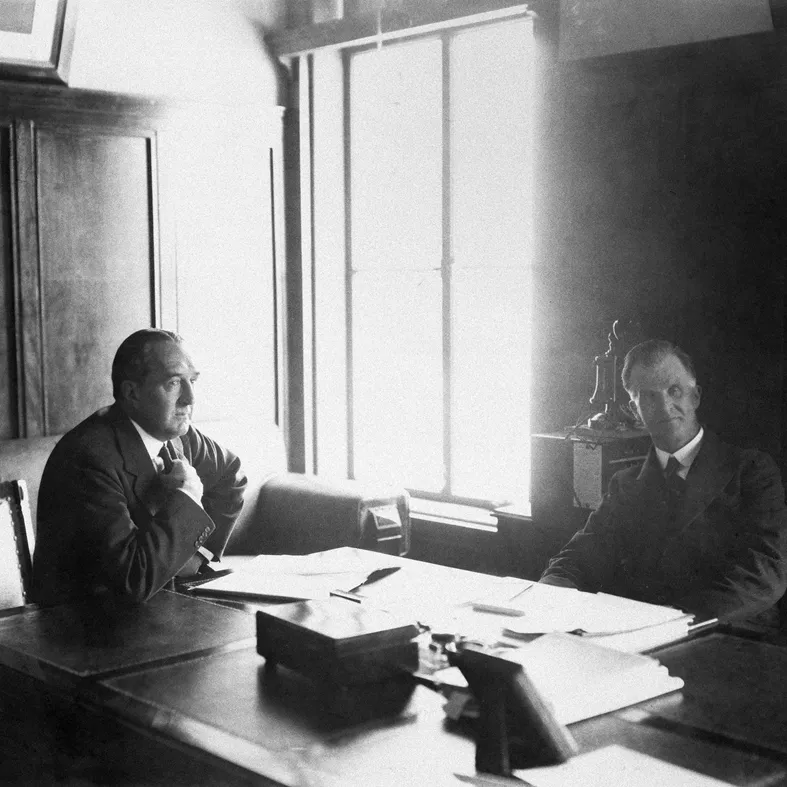 Bruce and Scullin sit at a large wooden desk