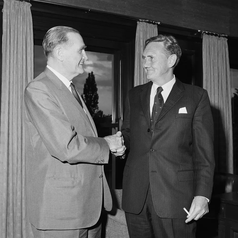 John McEwen shakes John Gorton's hand. Gorton is holding a cigarette.