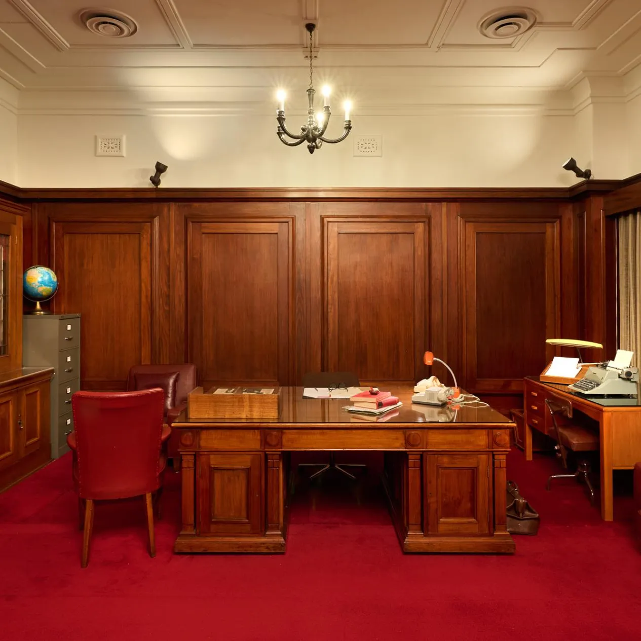 An office at Old Parliament House with red carpet, a large wooden desk, red leather chairs, wood panelled-walls and a book case.