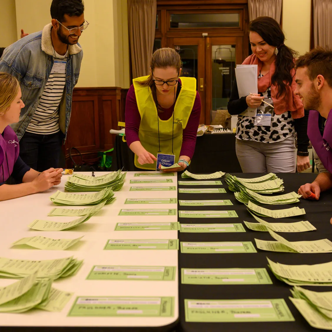 Officials in yellow and purple vests count green ballot paper votes on a table in Old Parliament House.