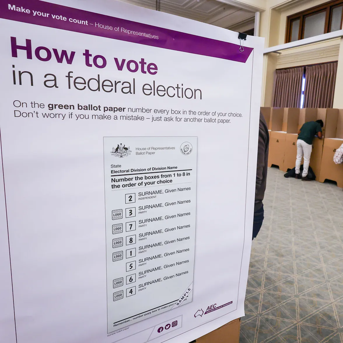 A large white poster with voting instructions for a federal election is displayed near cardboard polling booths in Old Parliament House.