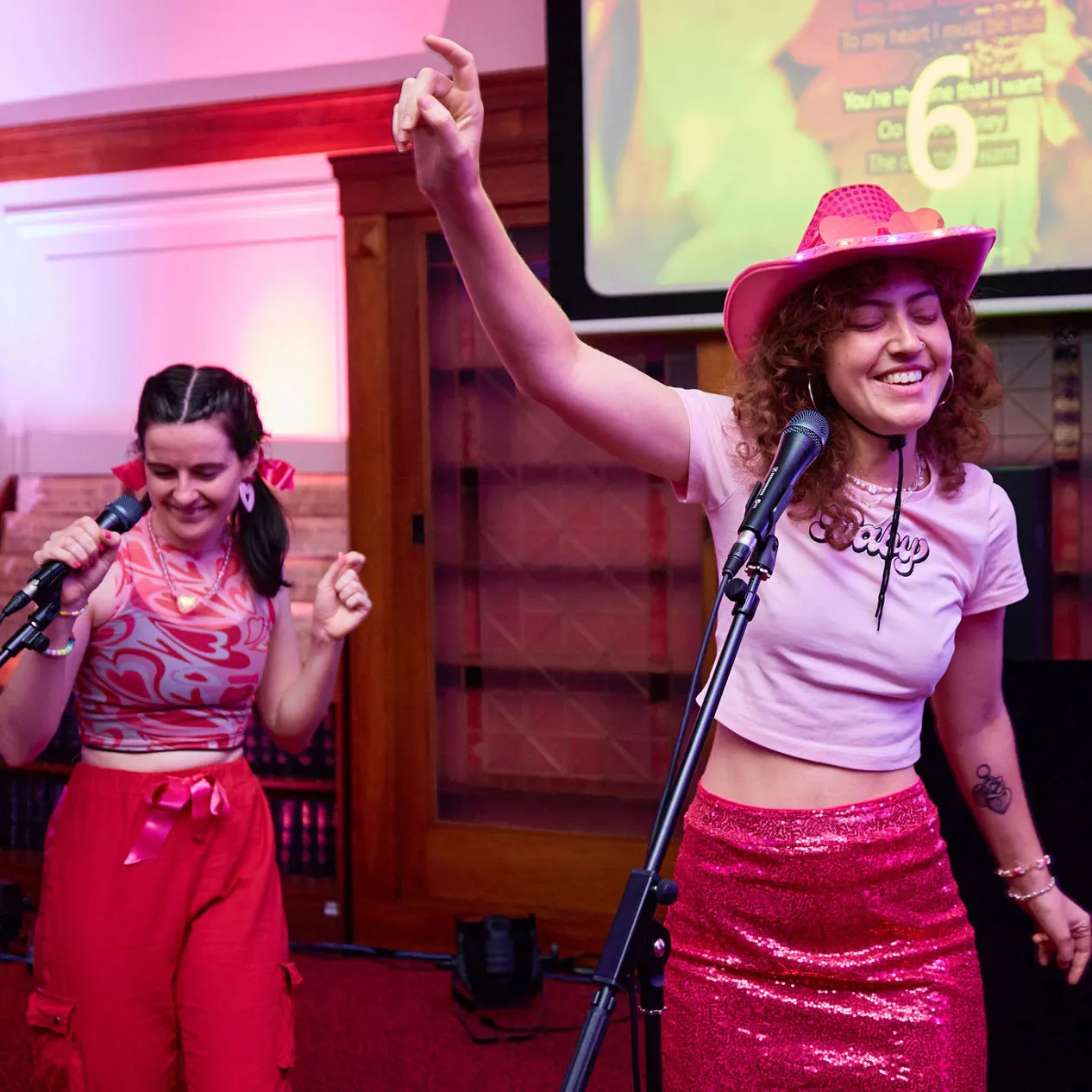 Two women wearing pink dance in front of microphones in Old Parliament House.