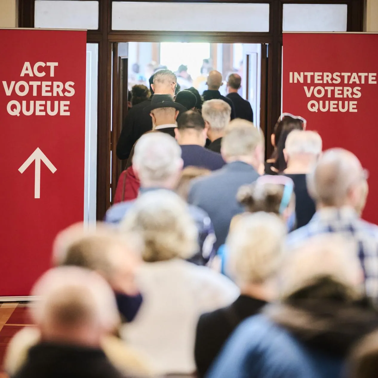 Two red banners, one directing ACT voters and one for interstate voters stand on either side of a doorway filled with people in Old Parliament House.