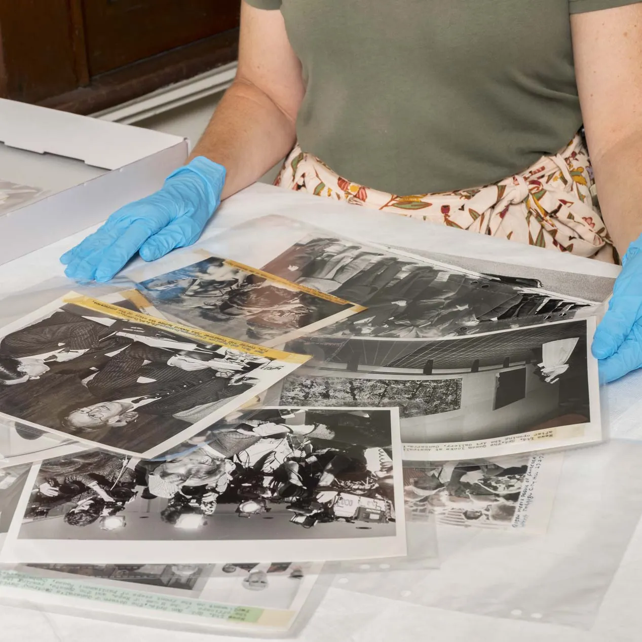 A person wearing blue gloves sorts black and white photographs on a desk. 