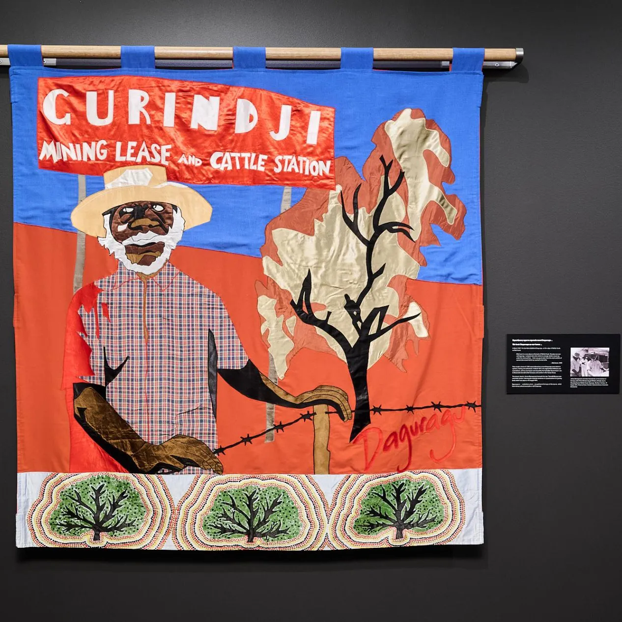 A Gurindji freedom banner depicting a First Nations person. The banner hangs in the exhibition on a black wall in Old Parliament House.