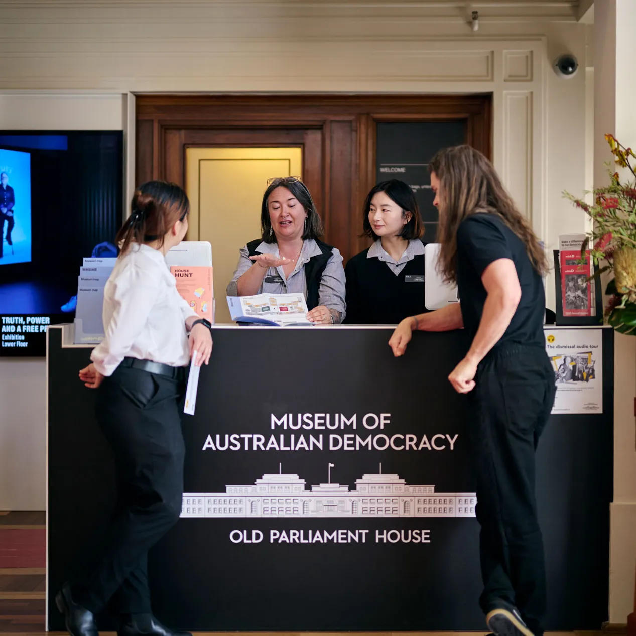 Museum staff show visitors to a brochure at the reception desk at MoAD at Old Parliament House.
