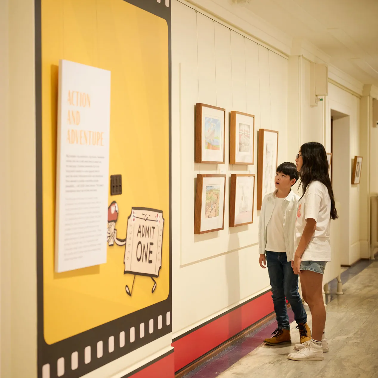 Two kids look at a wall of political cartoons in Old Parliament House.