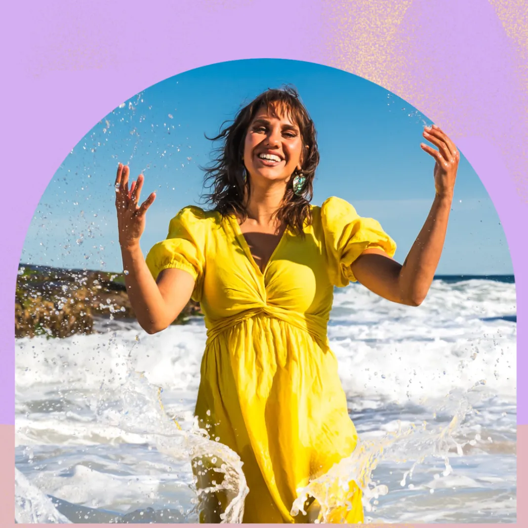 An image of Kirli Saunders playing in the water at a beach in front of an abstract background with block colours.