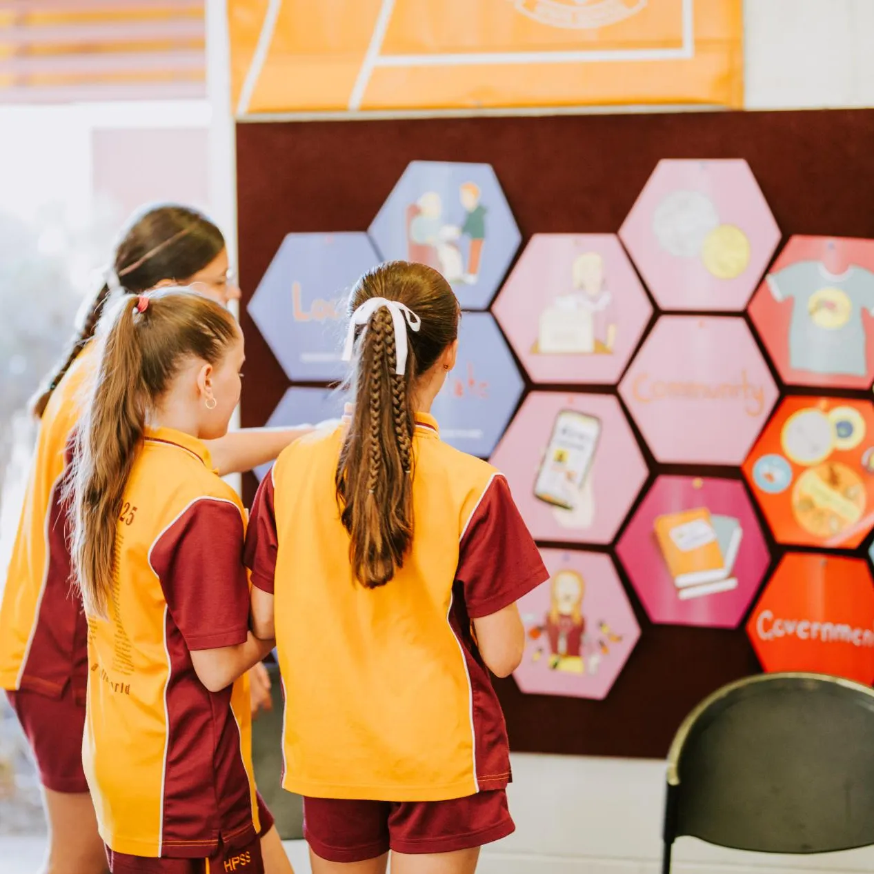 Three students in uniform looking at the hexagonal pieces of Democracy in a Box on the wall.
