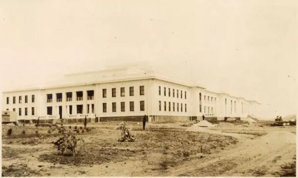 This sepia photograph depicts the undeveloped landscape around Parliament House in 1927 when the building first opened. The building sits in the centre of the image and to the left of the building are a few sad looking shrubs and the outline of the boundary of what would eventually become the House of Representatives Garden.