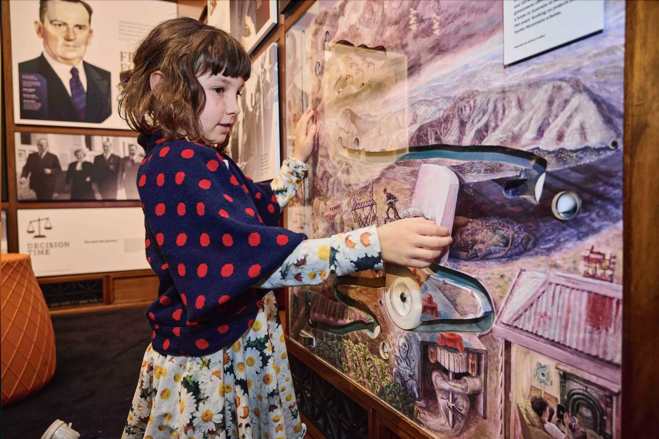 A young girl kneels on the floor and touches a marble display.