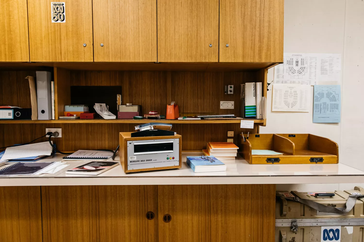 Brown old fashioned cupboard and desk with ABC stickers and the desktop covered in books, sticky tape and papers. 