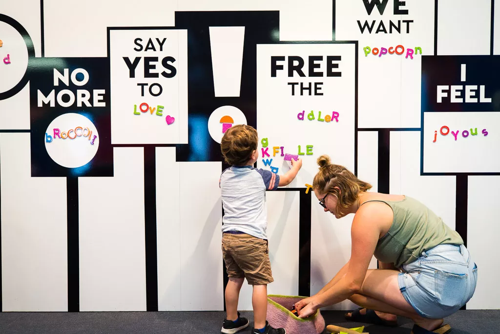 A small boy and his mother place magnets onto a wall with prompts such as 'say yes to love'.