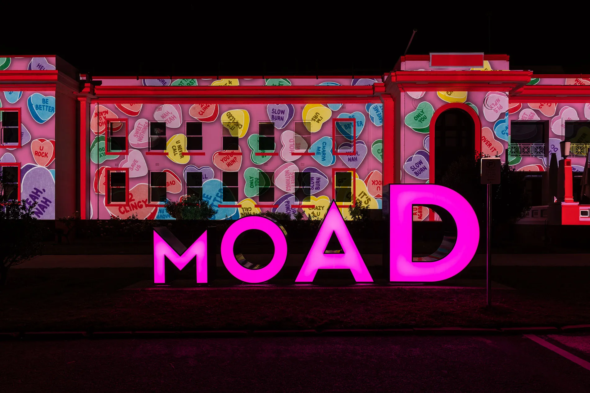 The MoAD sign illuminated in bright pink outside Old Parliament House, which has love hearts projected onto it.