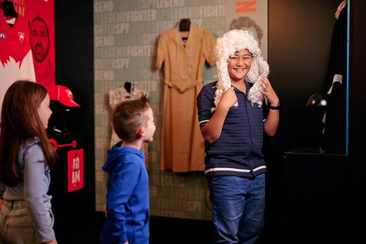 A child dressing up wearing a judge's wig while two other children look on and laugh.